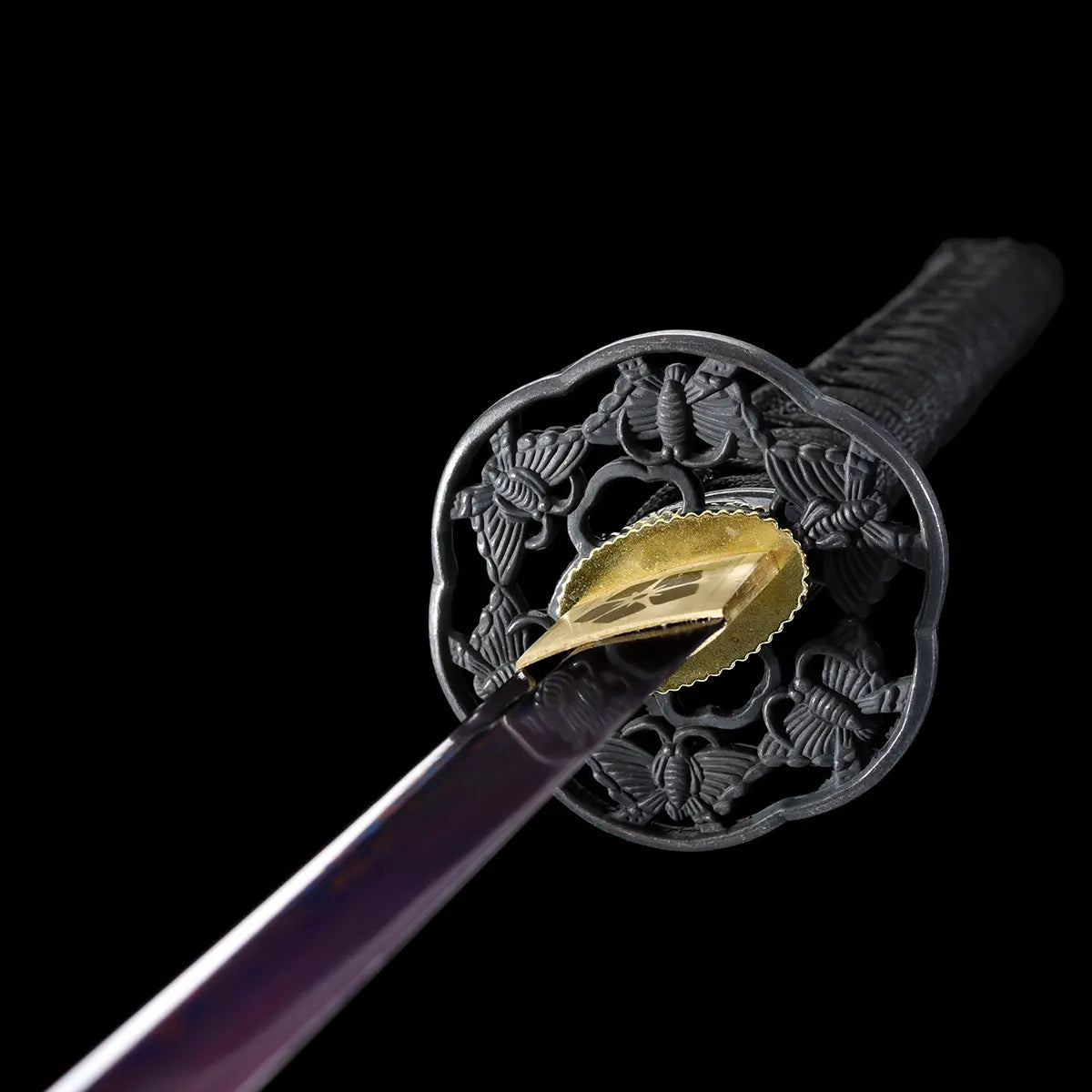 Vue rapprochée de la tsuba noire ciselée et du habaki doré gravé du katana japonais Tomoe Gozen.