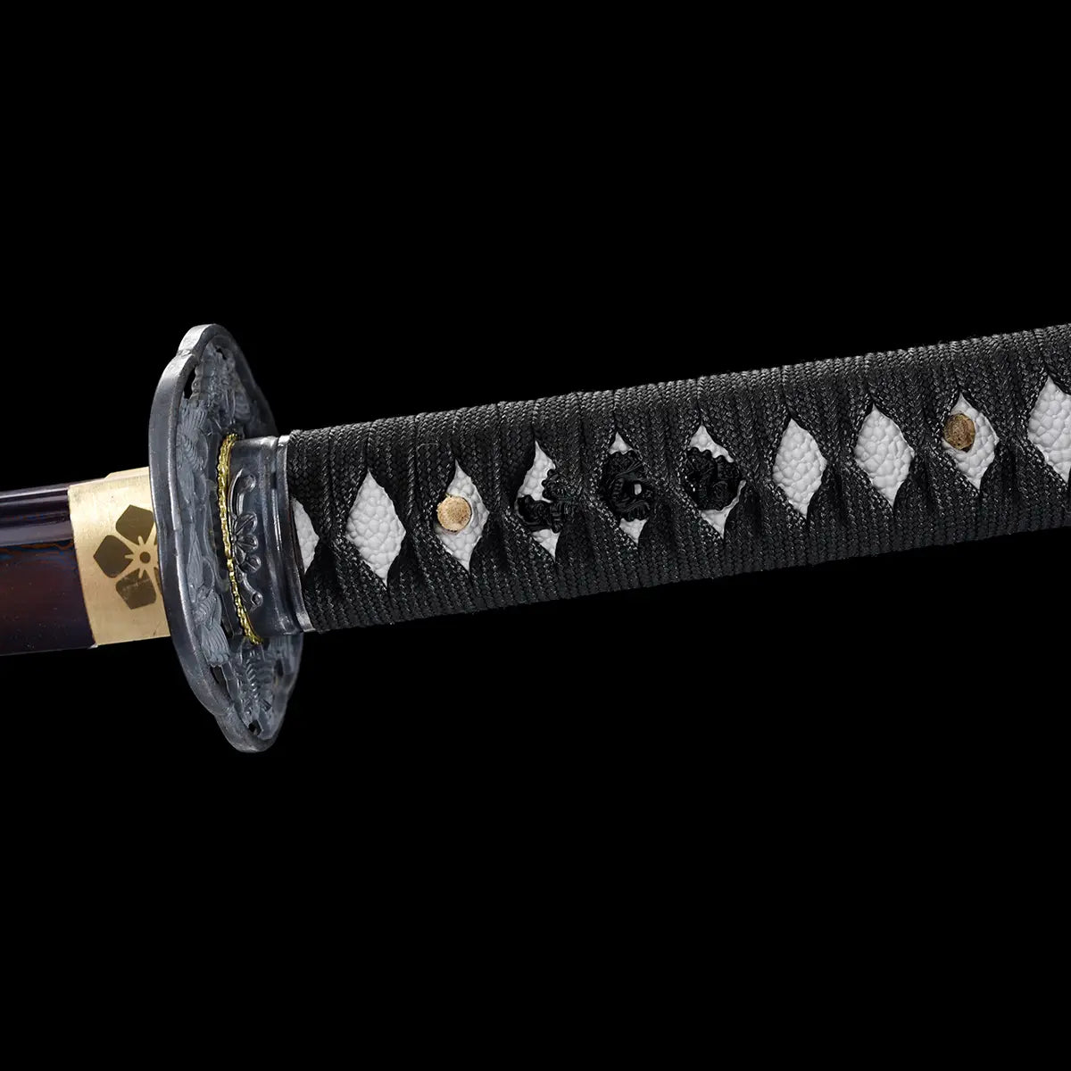 Gros plan sur la tsuka noire avec tressage traditionnel et incrustations du katana japonais Tomoe Gozen.