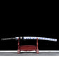 Katana japonais Tomoe Gozen avec saya blanc décoré de motifs bleus, présenté sur un support en bois, lame forgée 880 couches finition pourpre.