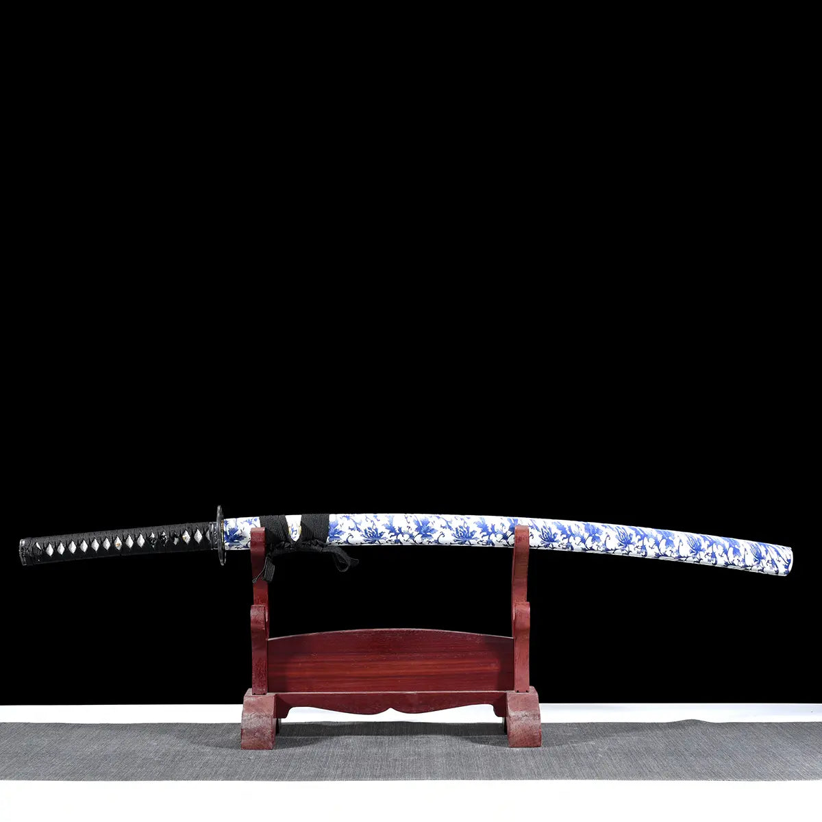 Katana japonais Tomoe Gozen avec saya blanc décoré de motifs bleus, présenté sur un support en bois, lame forgée 880 couches finition pourpre.
