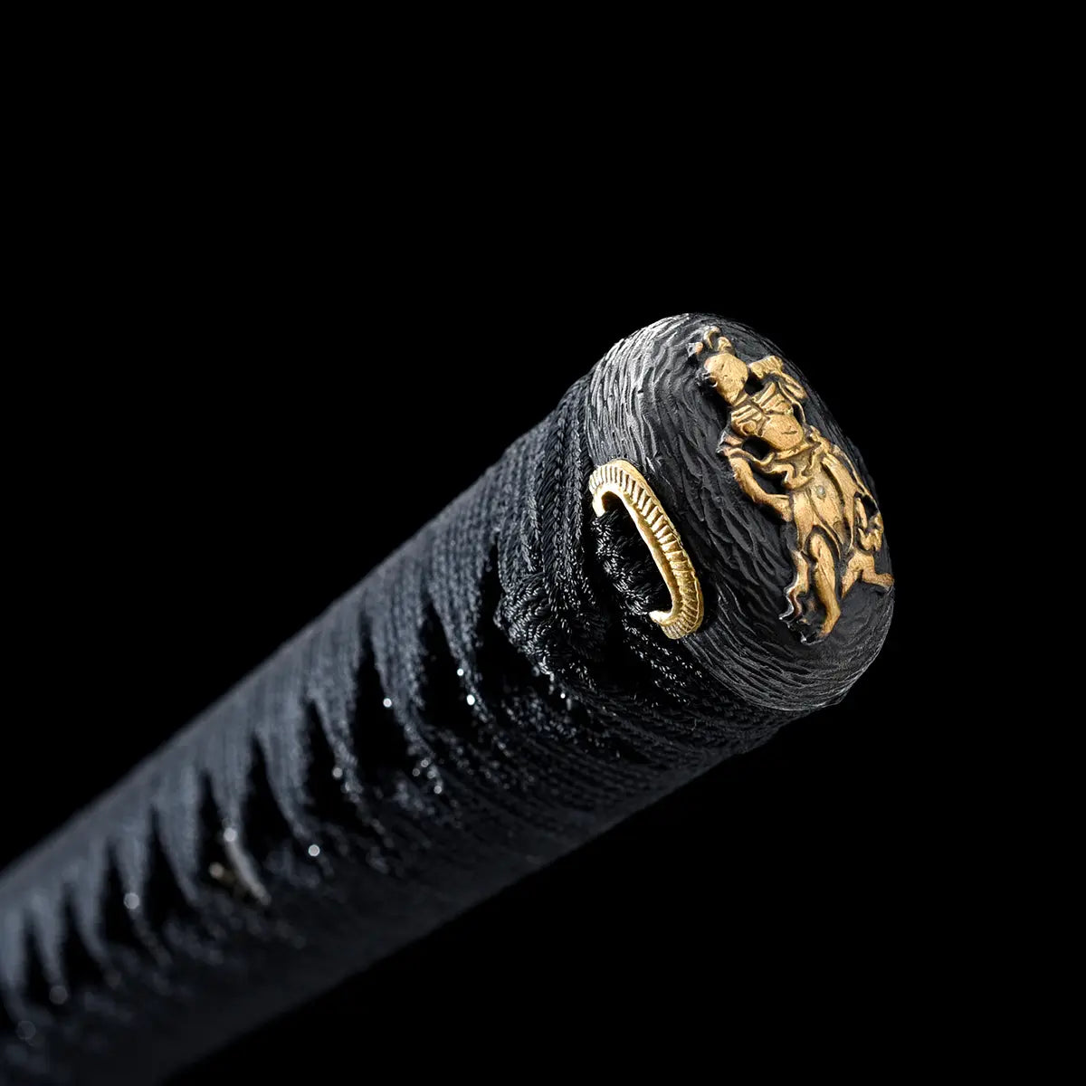 Close-up photograph of the end of a Japanese katana handle on a deep black background, highlighting the black kashira end cap decorated with a gold dragon motif, the black ito wrap tightly braided around the tsuka, and a gold cord ring detail, emphasizing traditional Japanese craftsmanship, premium materials, and refined samurai sword finishing.
