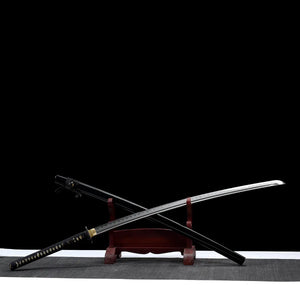 Katana nodachi “Monohoshizāo” artisanal, lame et saya croisés sur support en bois (acajou), hamon réel bien marqué, habaki laiton, tsuka noire à losanges ivoire, fond studio noir minimaliste et tapis gris — hommage à Sasaki Kojirō, esprit ōdachi élancé.