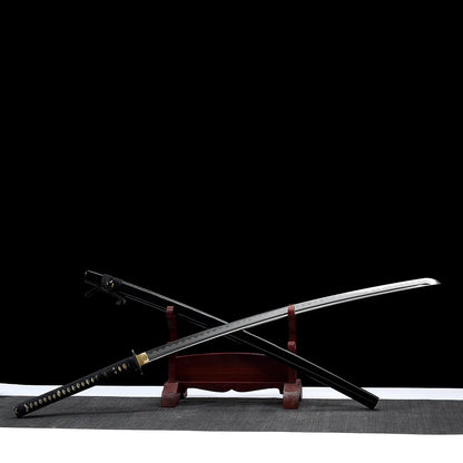 Katana nodachi “Monohoshizāo” artisanal, lame et saya croisés sur support en bois (acajou), hamon réel bien marqué, habaki laiton, tsuka noire à losanges ivoire, fond studio noir minimaliste et tapis gris — hommage à Sasaki Kojirō, esprit ōdachi élancé.