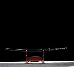 Katana nodachi Monohoshizāo, reproduction artisanale hommage à Sasaki Kojirō : vue entière dans son saya noir laqué, posé sur support en bois (teinte acajou), tsuka noire à losanges ivoire visibles, fond studio noir minimaliste, esprit ōdachi élégant.