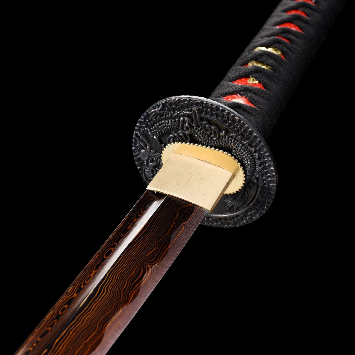 Gros plan sur la base de la lame du katana japonais Ryū Honō, acier damas rouge-feu avec tsuba noire ornée d’un dragon et habaki doré. Poignée tsuka noire tressée de rouge sur fond noir studio Blade Bushido, illustrant la finesse du travail de forge et la symbolique du dragon de flamme.