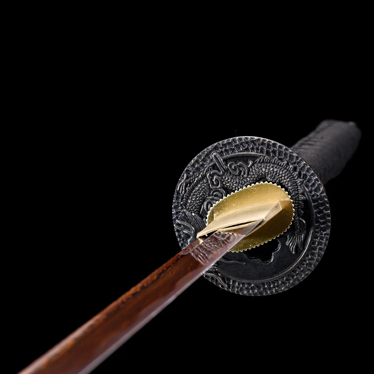 Vue rapprochée sur la tsuba du katana japonais Ryū Honō, garde noire gravée d’un dragon en relief, lame damas rouge et habaki doré. Photographie sur fond noir studio Blade Bushido mettant en valeur le travail du métal et la symbolique du dragon de flamme.