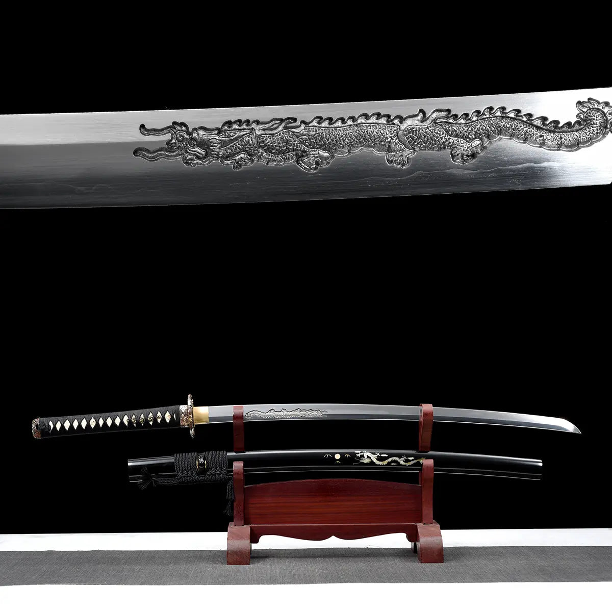 Composition double montrant le katana japonais artisanal Ryū no Ken sur fond noir, avec en partie supérieure un gros plan de la lame en acier poli présentant une longue gravure dragon en relief, et en partie inférieure le katana dégainé exposé sur un support en bois verni rouge, fourreau noir laqué décoré d’un motif dragon placé en dessous, manche noir tressé avec losanges blancs en peau de raie, habaki doré visible, surface inférieure gris clair, mise en scène mettant en valeur à la fois le détail de la gr