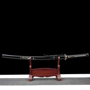 Vue complète du katana japonais artisanal Ryū no Ken présenté sur un support en bois verni rouge, photographié sur fond noir avec surface inférieure gris clair, lame rangée dans son fourreau noir laqué décoré d’un motif dragon, manche noir tressé avec losanges blancs en peau de raie, garde décorative visible, sabre posé horizontalement sur le présentoir, composition frontale mettant en valeur l’ensemble du katana et son support.
