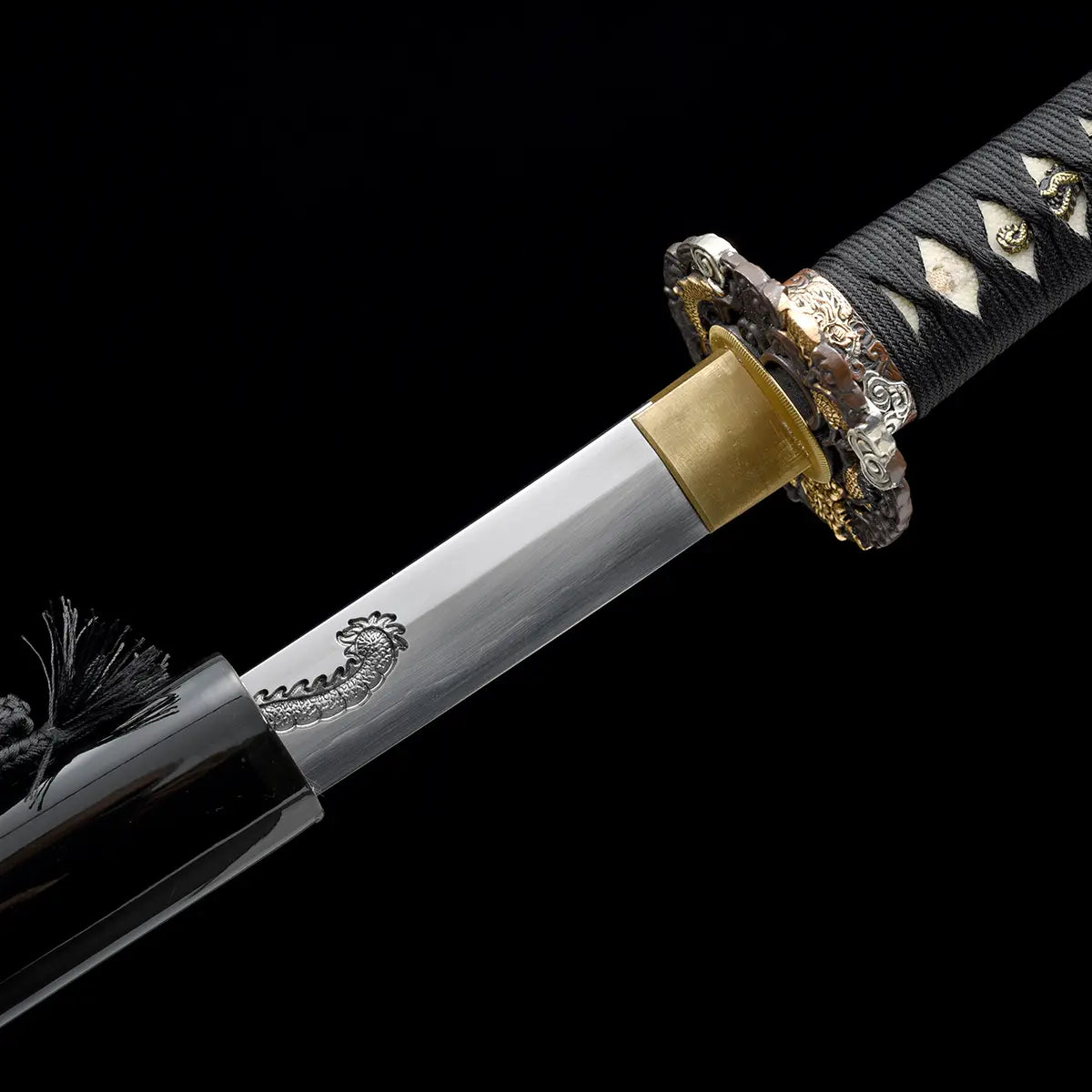Vue rapprochée de la jonction entre la lame et le fourreau du katana japonais artisanal Ryū no Ken sur fond noir uniforme, lame en acier poli avec gravure dragon visible près de la base, habaki en laiton doré ajusté avec précision, saya noir laqué partiellement visible avec cordon noir, manche noir tressé avec losanges blancs en peau de raie en arrière-plan, absence de support, cadrage diagonal mettant en valeur l’ajustement et la finition des éléments.
