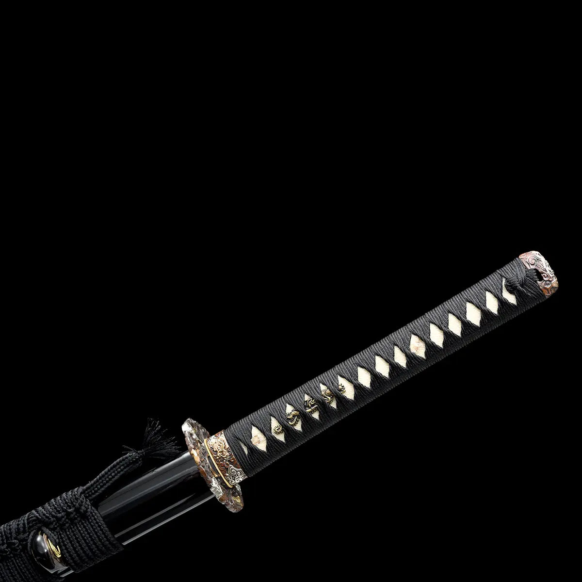 Vue complète du manche du katana japonais artisanal Ryū no Ken sur fond noir uniforme, tsuka noire entièrement tressée avec losanges blancs en peau de raie apparente et ornements métalliques décoratifs intégrés, tsuba ronde sculptée visible à la jonction, fourreau noir laqué présent sur la partie gauche avec cordon noir, absence de support, cadrage diagonal mettant en valeur la longueur du manche et la régularité du tressage.
