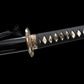 Détail du manche du katana japonais artisanal Ryū no Ken sur fond noir profond, tsuka noire tressée avec losanges blancs en peau de raie apparente et ornements métalliques décoratifs, tsuba ronde partiellement visible avec finitions sculptées, fourreau noir laqué présent à gauche avec cordon noir, absence de support, cadrage horizontal mettant en valeur la texture du tressage et la qualité des ajustements.

