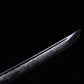 Close-up of Japanese katana Sakura no Ken blade tip, black background, unsheathed black steel blade with engraved sakura floral pattern along the edge, visible curved kissaki, decorative engraving details highlighted on the blade surface
