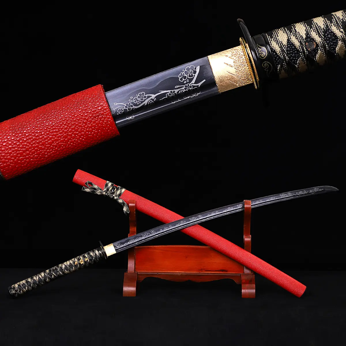 Full view of Japanese katana Sakura no Ken displayed on a wooden stand, black background, unsheathed black steel blade with engraved sakura floral pattern, red leather wrapped saya positioned diagonally, black and white tsuka handle visible, traditional samurai sword presentation with strong contrast between blade and scabbard
