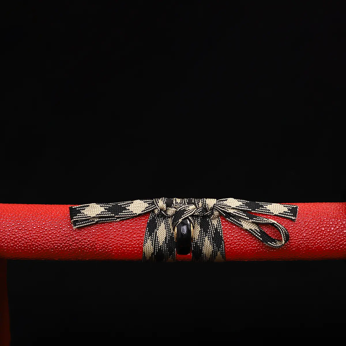 Close-up of Japanese katana Sakura no Ken saya, black background, red leather wrapped scabbard with textured surface, black and white woven sageo tied around the saya, detailed knot visible, traditional samurai sword mounting
