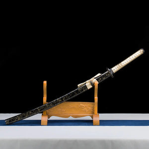 Katana japonais Toyotomi Hideyoshi posé sur un support en bois sculpté, saya noir laqué or et tsuka doré tressé. Photographie d’exposition sur fond noir avec base blanche et tissu bleu, studio Blade Bushido.