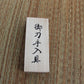 Couvercle de coffret en bois clair avec kanji noirs, posé sur tatami tressé beige/brun, vue de dessus, lumière douce — coffret de rangement du kit d’entretien katana, accessoires de maintenance pour sabre japonais.