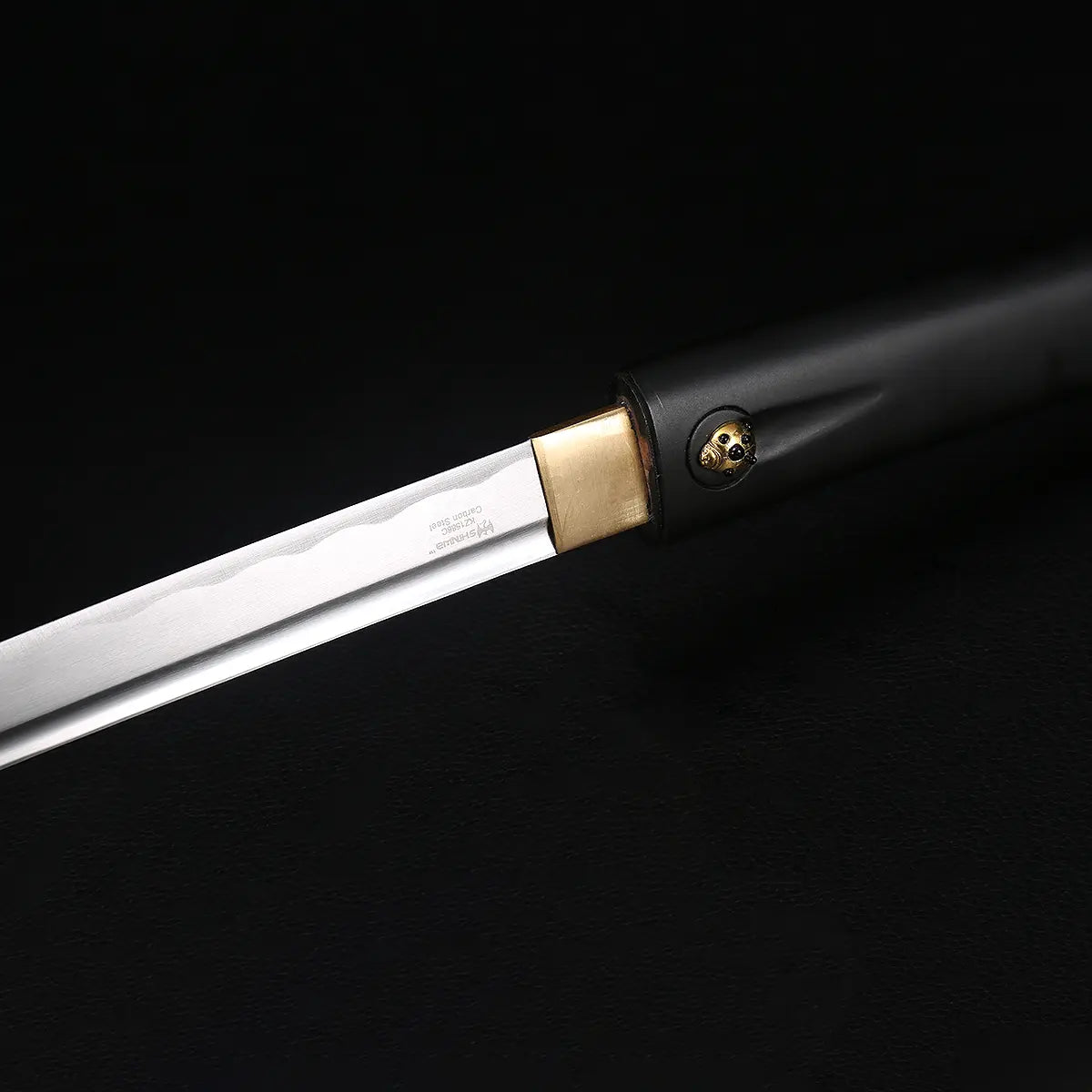Détail de la lame du katana shirasaya noir KUROTAKE partiellement sortie du fourreau, photographié sur fond noir, montrant l’acier poli avec ligne de trempe discrète, l’habaki en laiton, ainsi que la poignée en bois dur laqué noir imitation bambou avec insert décoratif visible, ensemble sans tsuba.

