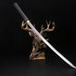 Katana shirasaya noir KUROTAKE avec la lame sortie du fourreau, présenté en diagonale sur un support décoratif en forme de tête de cerf, fond noir profond, lame en acier poli visible sur toute sa longueur, fourreau et poignée en bois dur laqué noir imitation bambou, habaki en laiton apparent, ensemble sans tsuba.

