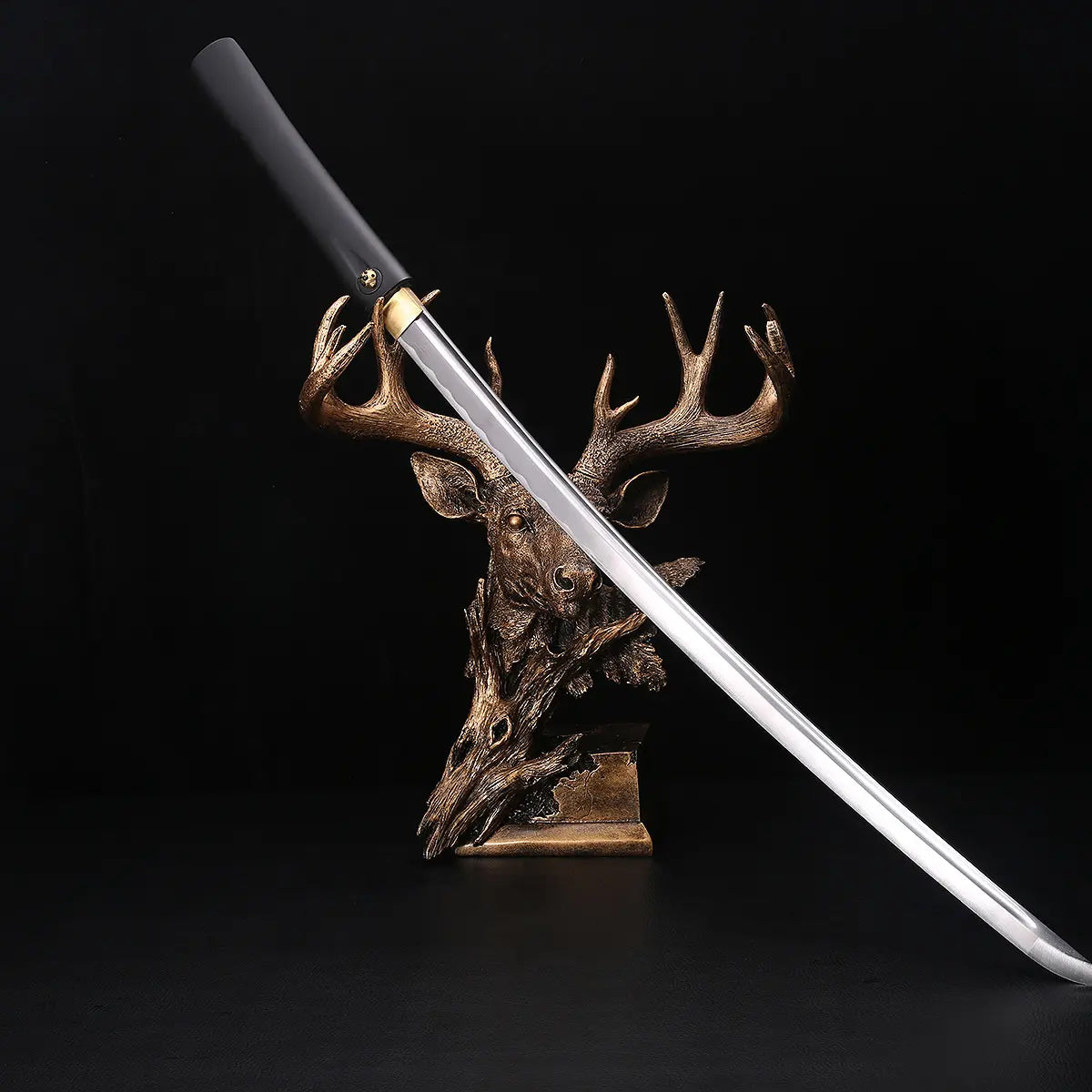 Katana shirasaya noir KUROTAKE avec la lame sortie du fourreau, présenté en diagonale sur un support décoratif en forme de tête de cerf, fond noir profond, lame en acier poli visible sur toute sa longueur, fourreau et poignée en bois dur laqué noir imitation bambou, habaki en laiton apparent, ensemble sans tsuba.
