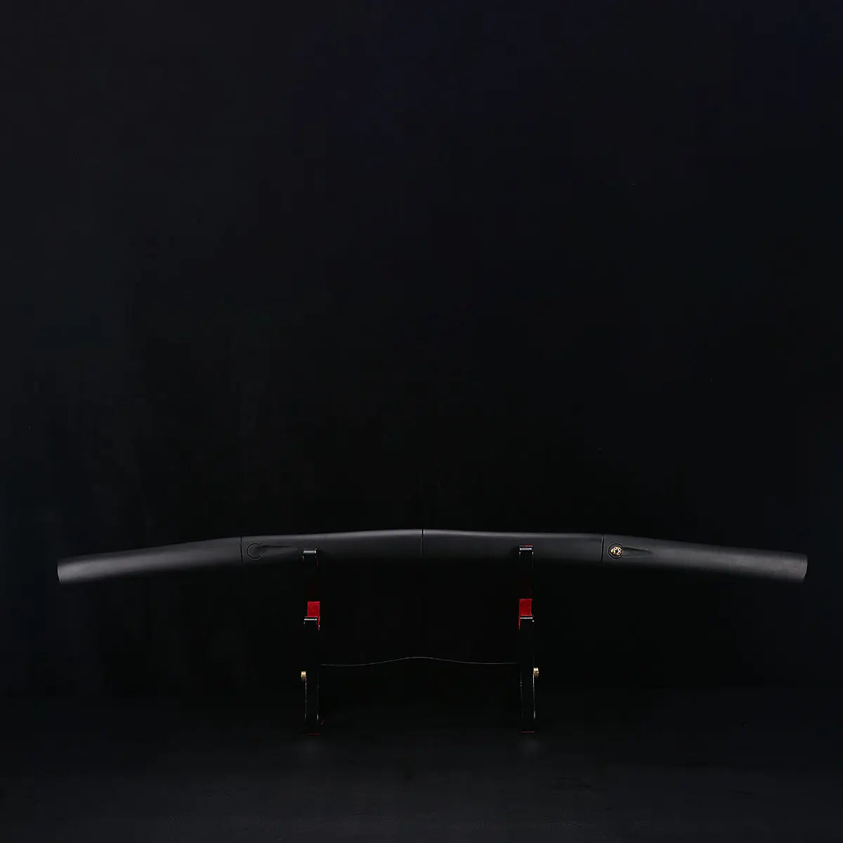 Katana shirasaya noir KUROTAKE posé sur un support en bois sombre, photographié sur fond noir, montrant le fourreau et la poignée en bois dur laqué noir imitation bambou, ligne courbe du saya visible, insert décoratif discret sur la poignée, présentation horizontale sans tsuba.
