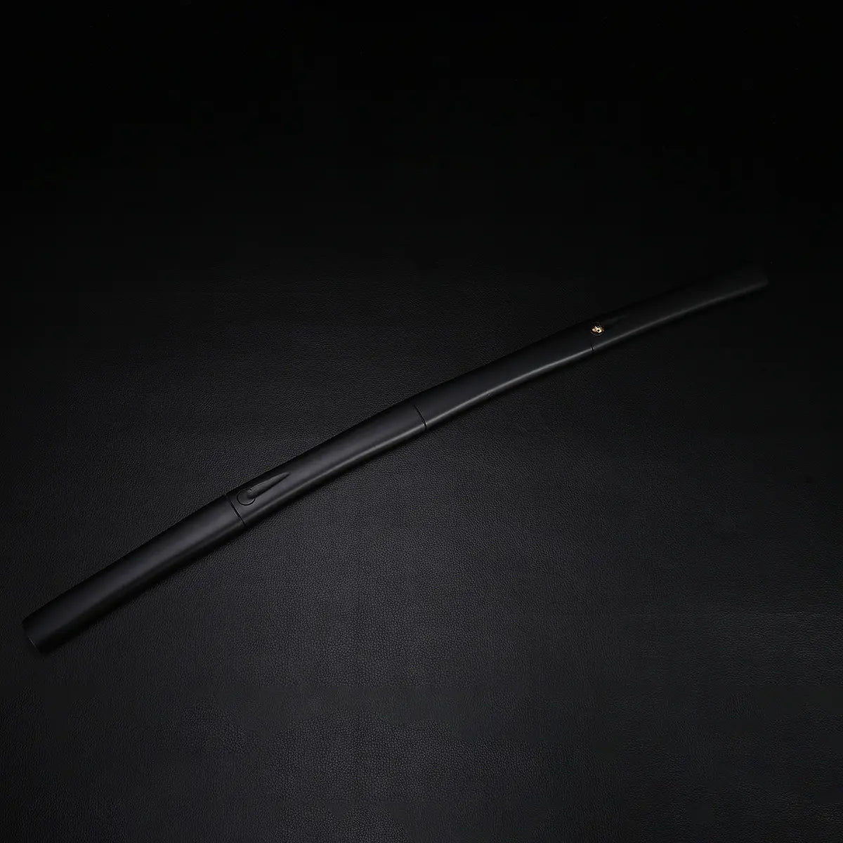 Fourreau du katana shirasaya noir KUROTAKE photographié seul sur fond noir texturé, montrant la courbure naturelle du saya en bois dur laqué noir imitation bambou, finition mate uniforme, absence de tsuba, ligne épurée et jonctions discrètes visibles.
