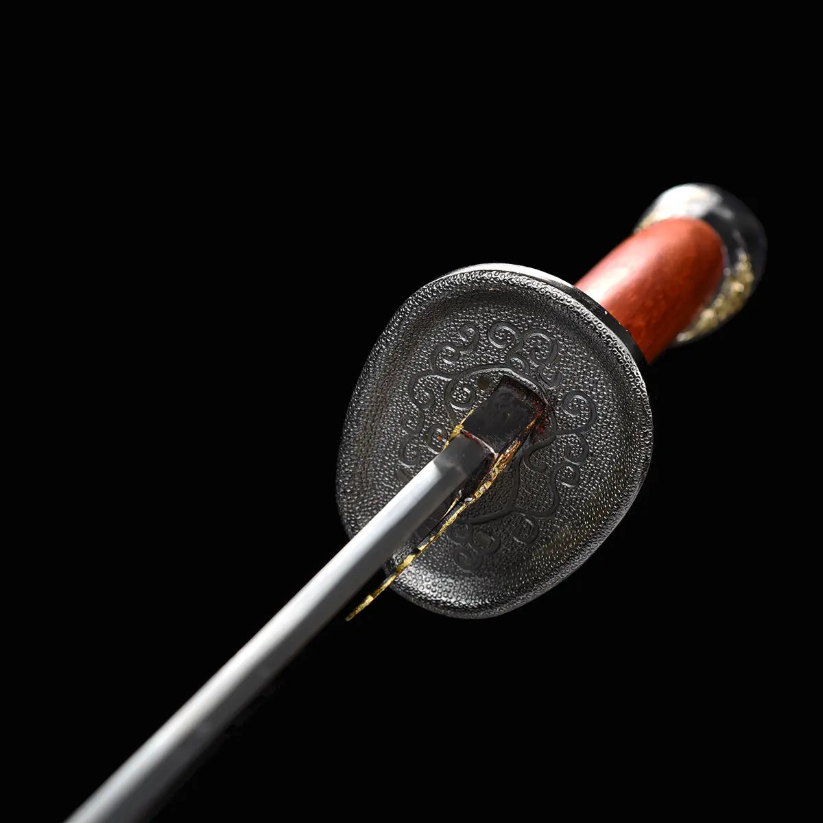 Gros plan sur la garde noire gravée du sabre chinois Dao LONG FENG, avec lame partiellement visible, poignée rouge-brun en bois, pommeau décoré en arrière-plan et fond noir sobre.