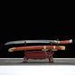 Sabre chinois Dao LONG FENG avec lame courbe sortie du fourreau, présenté sur un support en bois devant un fond noir, avec fourreau rouge-brun, poignée assortie, garde noire, garnitures dorées sculptées et chaînes décoratives visibles.
