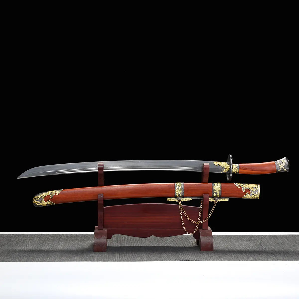 Sabre chinois Dao LONG FENG avec lame courbe sortie du fourreau, présenté sur un support en bois devant un fond noir, avec fourreau rouge-brun, poignée assortie, garde noire, garnitures dorées sculptées et chaînes décoratives visibles.