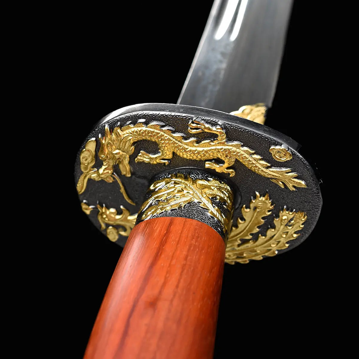 Gros plan sur la garde noire et dorée du sabre chinois Dao LONG FENG, avec motifs dragon et phénix en relief, poignée rouge-brun en bois, lame courbe partiellement visible en arrière-plan et fond noir sobre.