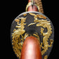 Gros plan frontal sur la garde du sabre chinois Dao LONG FENG, avec motifs dragon et phénix dorés en relief sur fond noir texturé, poignée rouge-brun en bois et lame partiellement visible en arrière-plan.
