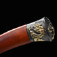 Gros plan sur le pommeau du sabre chinois Dao LONG FENG, avec poignée rouge-brun en bois, garniture noire texturée, motif dragon doré en relief et fond noir sobre.