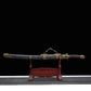 Sabre chinois Dao LONG WEI présenté dans son fourreau noir texturé sur un support en bois rouge, avec poignée brune tressée, garde ronde en laiton, garnitures dorées à motifs de dragon et fond noir.