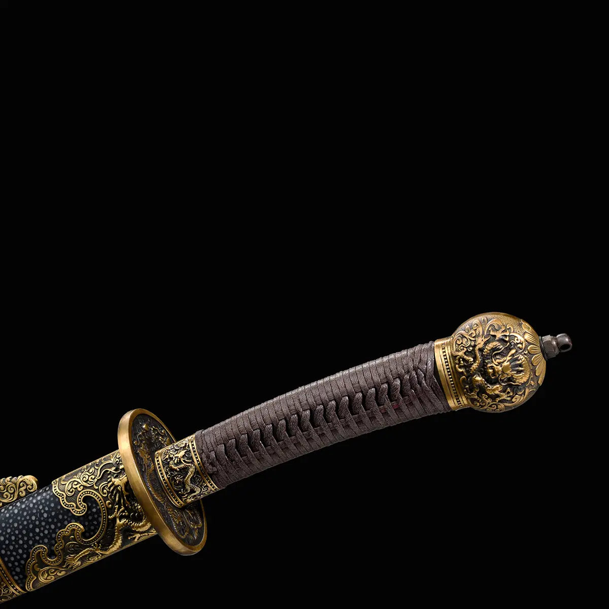 Gros plan sur la poignée brune tressée du sabre chinois Dao LONG WEI, avec pommeau décoré en laiton, garde ronde ornée de dragons et partie du fourreau noir texturé avec garnitures dorées sur fond noir.