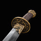 Gros plan sur la garde ronde en laiton du sabre chinois Dao LONG WEI, avec motifs dragon dorés, poignée brune tressée, pommeau décoré et base de lame courbe argentée visible sur fond noir.