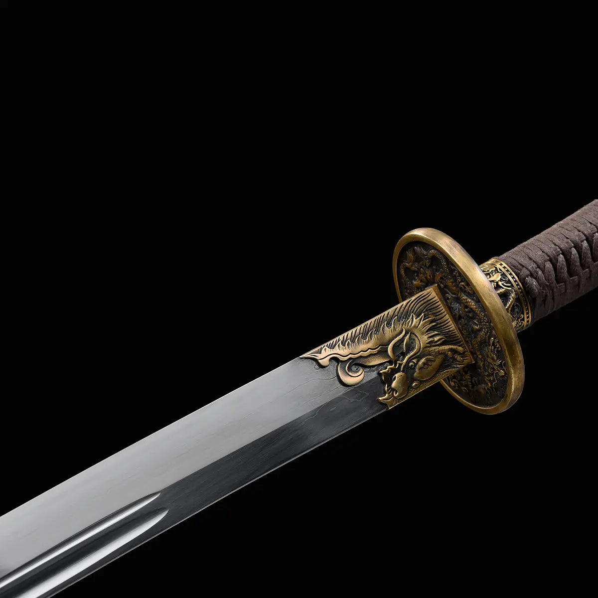 Gros plan sur le sabre chinois Dao LONG WEI avec lame courbe argentée, gorge centrale, garde ronde en laiton décorée de motifs dragon, poignée tressée brune et ornements dorés sur fond noir.