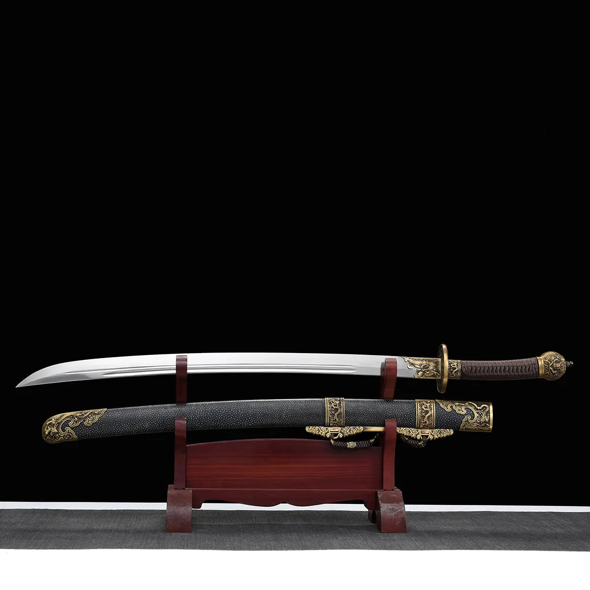 Sabre chinois Dao LONG WEI présenté hors de son fourreau noir texturé sur un support en bois rouge, avec lame courbe argentée, gorge centrale, poignée brune tressée, garde ronde en laiton et garnitures dorées à motifs dragon sur fond noir.