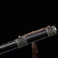 Détail du fourreau d’une épée chinoise Jian Longquan, avec bois sombre type ébène, garnitures métalliques ornementées, cordon brun, pompon traditionnel et fond noir.