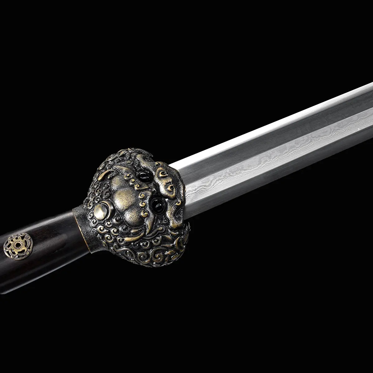 Gros plan sur la garde ouvragée d’une épée chinoise Jian Longquan, avec lame droite en acier plié à motif apparent, poignée sombre, garnitures métalliques décorées et fond noir.
