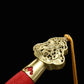 Gros plan sur le pommeau doré ouvragé de l’épée chinoise Jian LONGQUAN HONG LONG, avec poignée rouge texturée, garniture en laiton, dragonne jaune et motifs sculptés visibles sur fond noir.