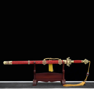 Épée chinoise Jian LONGQUAN HONG LONG présentée dans son fourreau rouge texturé sur un support en bois, avec garnitures dorées, garde traditionnelle ouvragée, poignée rouge et dragonne à pompon jaune sur fond noir.