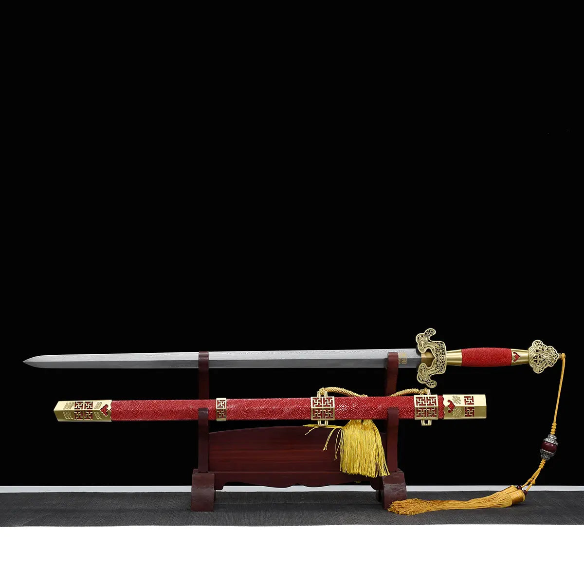 Épée chinoise Jian LONGQUAN HONG LONG présentée avec sa lame droite sortie du fourreau rouge, posée sur un support en bois devant un fond noir, avec garde dorée ouvragée, poignée rouge, garnitures en laiton et dragonne à pompon jaune.