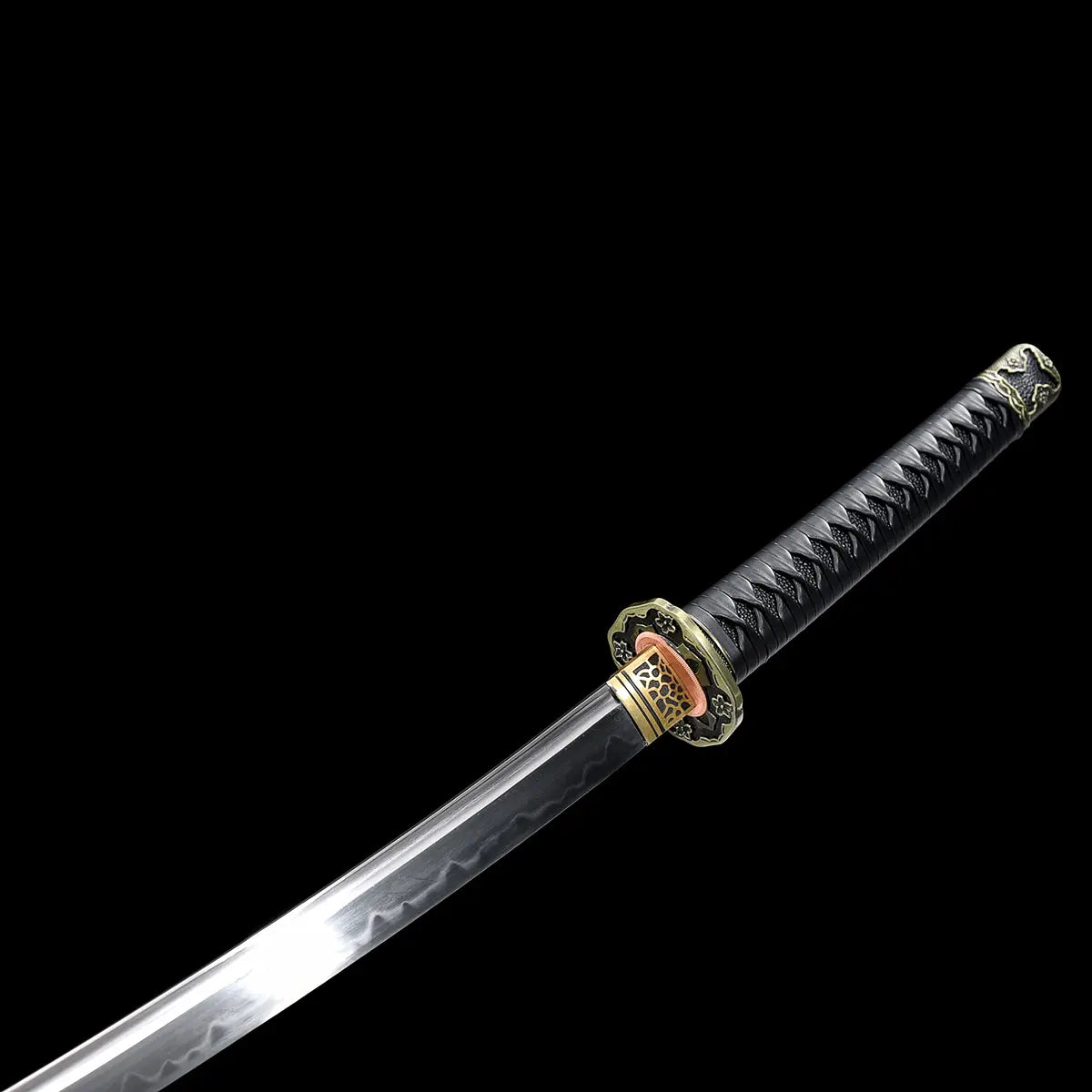 Partial view of the Japanese katana Meiyo on a solid black background, showing the polished T10 steel blade together with the handle assembly. The image highlights the real wavy hamon along the cutting edge, the brass habaki at the base of the blade, and the round tsuba with antique-style floral decoration. The tsuka is wrapped in black ito over black rayskin, with the blade angled diagonally across the frame. No scabbard or stand is visible
