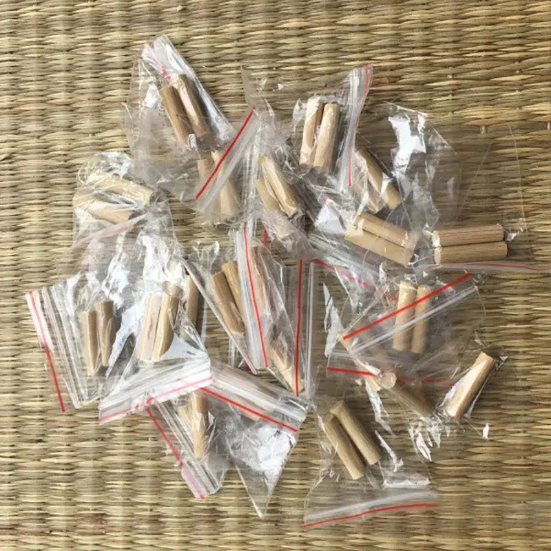 Plusieurs sachets zip transparents contenant des mekugi en bambou clair, posés en vrac sur un tatami tressé beige ; aucun sabre ni fourreau visible. Accessoires mekugi bambou katana, HEMA AMHE, vue de dessus.
