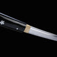 Close-up view of a Japanese cosplay katana showing the transition between the polished steel blade and the glossy black lacquered scabbard. A brass habaki is fitted at the blade base, with silver cherry blossom motifs visible on the black saya. The image is shot on a solid black background, with the sheath present and a minimalist shirasaya design without guard.
