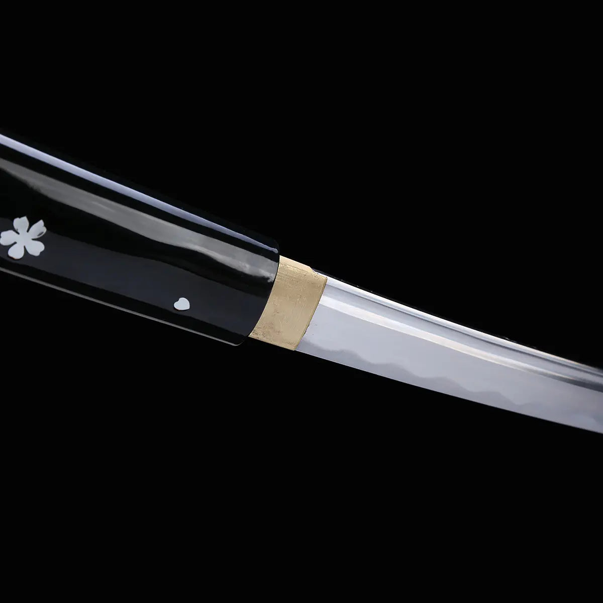 Close-up view of a Japanese cosplay katana showing the transition between the polished steel blade and the glossy black lacquered scabbard. A brass habaki is fitted at the blade base, with silver cherry blossom motifs visible on the black saya. The image is shot on a solid black background, with the sheath present and a minimalist shirasaya design without guard.
