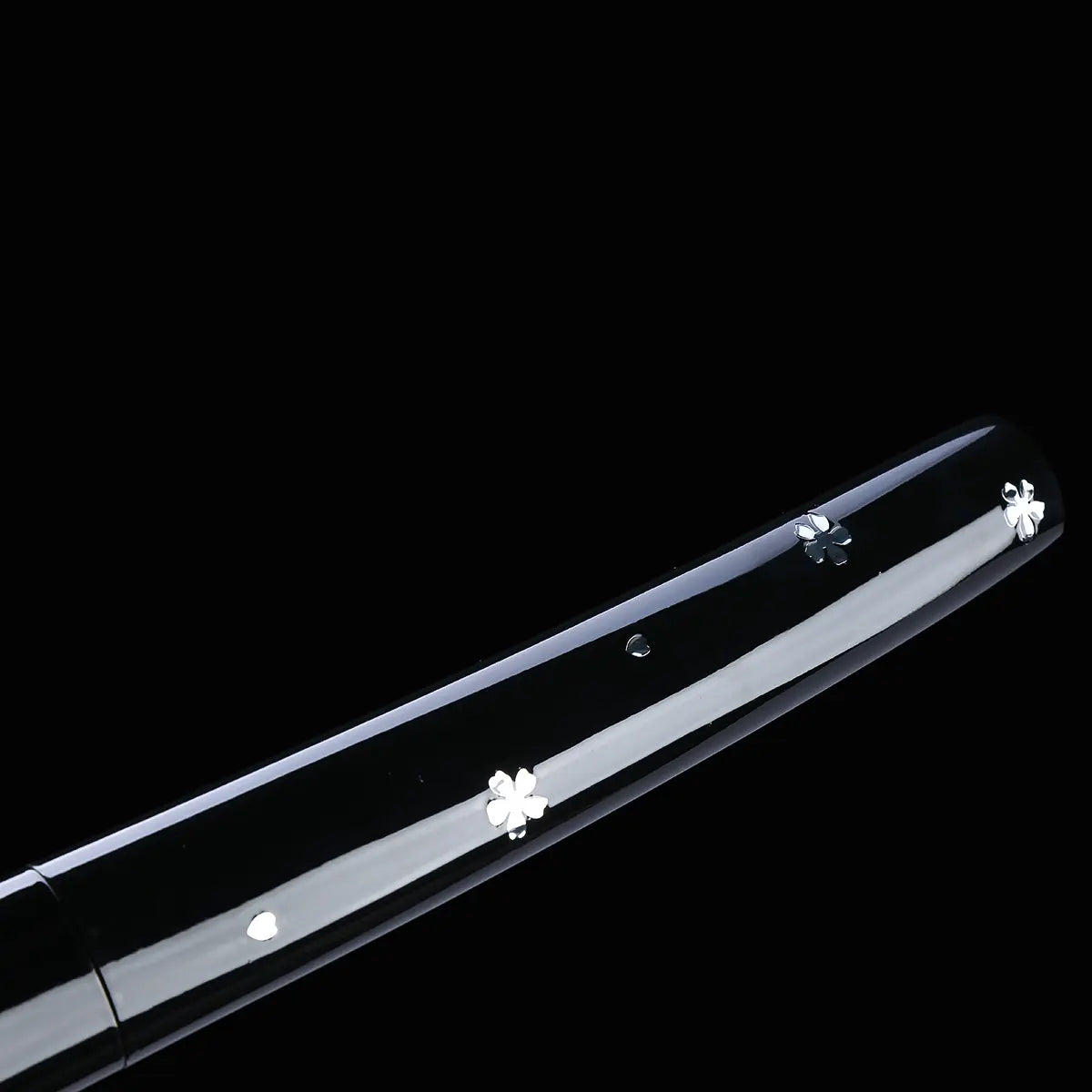 Detailed view of a Japanese cosplay katana shirasaya with a glossy black lacquered scabbard shown on a deep black background. The saya is decorated with silver cherry blossom motifs and a visible wooden seam line. The sheath is present, with no guard, highlighting a minimalist shirasaya design inspired by Japanese cinema.
