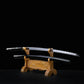 Full view of a Japanese cosplay katana displayed horizontally on a carved wooden stand against a solid black background. The katana features a glossy black lacquered shirasaya scabbard with silver cherry blossom motifs, with the polished steel blade partially visible above the saya. The sheath is present, no guard is visible, and the sword is positioned for decorative presentation.
