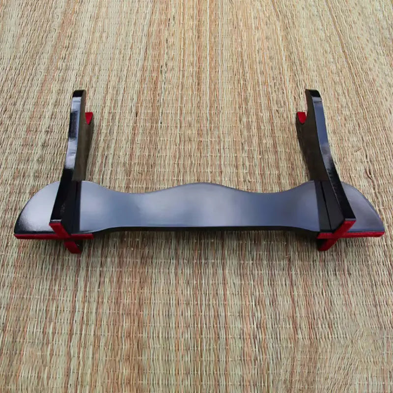Support de katana en bois laqué noir posé sur un tapis en fibres naturelles, montrant la structure complète du porte-katana avec courbes lisses, finitions brillantes et touches rouges sur les encoches, kake japonais destiné à exposer un sabre comme katana, wakizashi ou shirasaya.