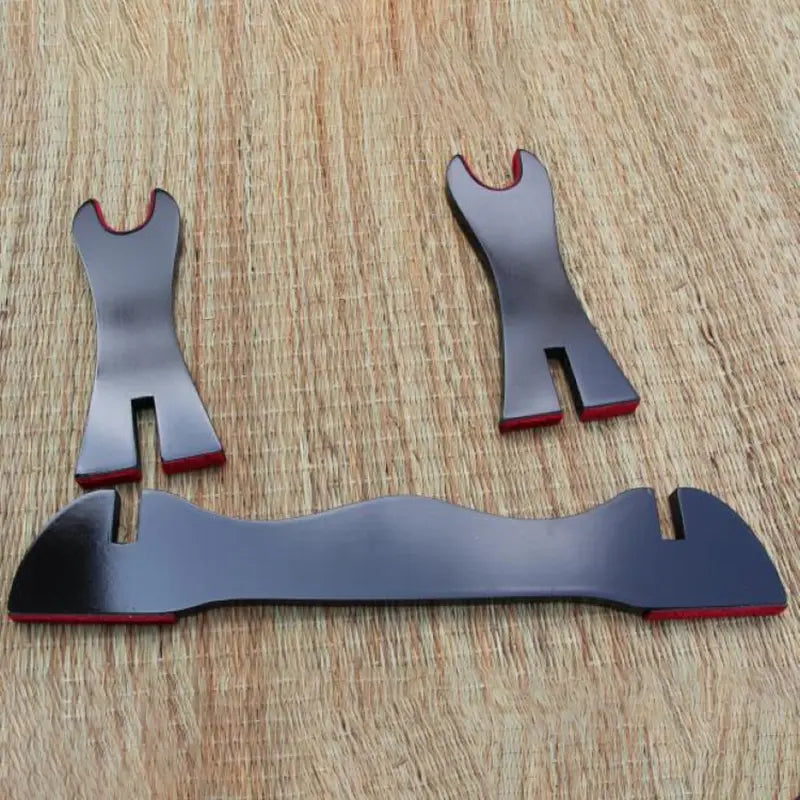 Éléments d’un présentoir pour katana en bois noir laqué posés sur un tapis en fibres naturelles, montrant les deux montants latéraux aux encoches rouges et la base courbe, illustrant les pièces du kake japonais avant assemblage pour exposer un sabre traditionnel.