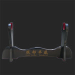 Présentoir pour katana en bois laqué noir, modèle Hattori Hanzo, photographié sur un fond noir uni, montrant le support brillant avec inscription dorée et protections rouges, utilisé comme support de sabre japonais, kake décoratif pour exposer katana, wakizashi ou shirasaya.